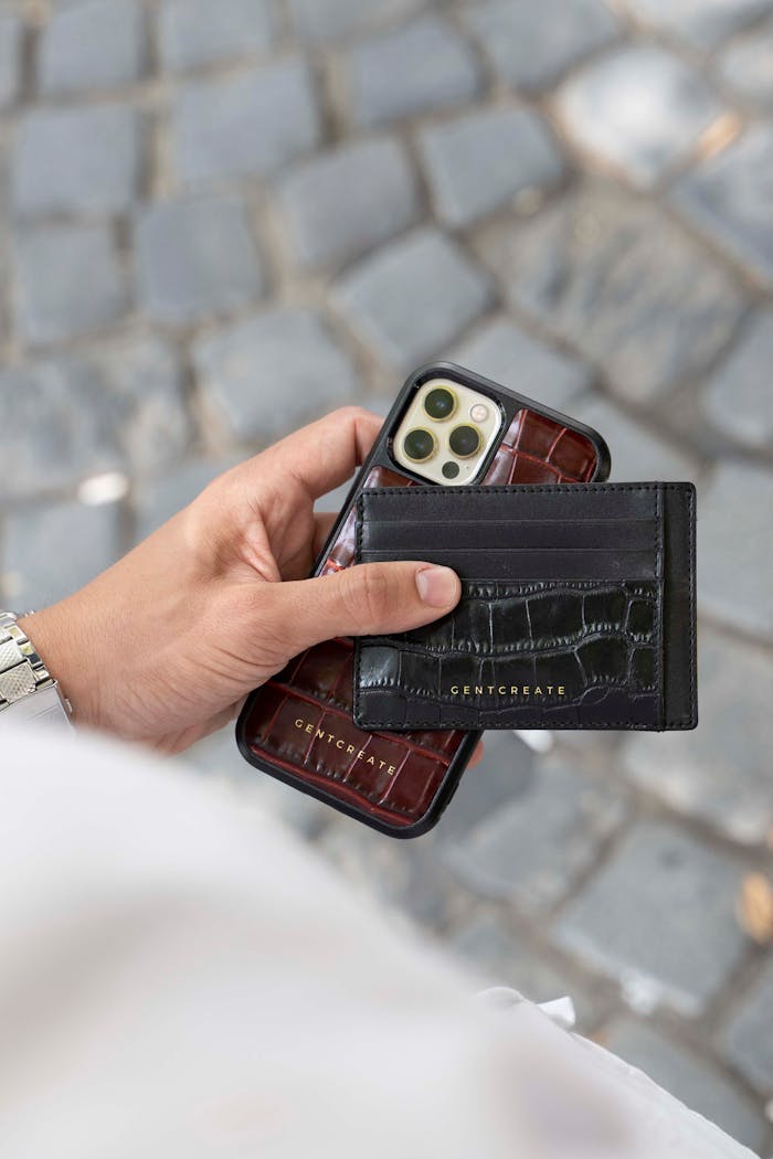 Person holding an iPhone with a black leather card holder on a paved street.