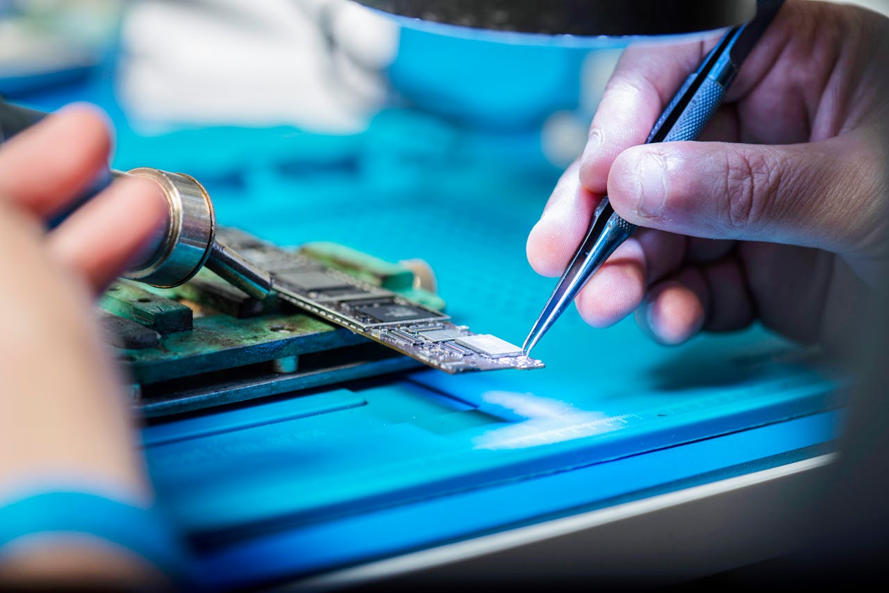 Hands delicately holding tools repairing a circuit board with precision.
